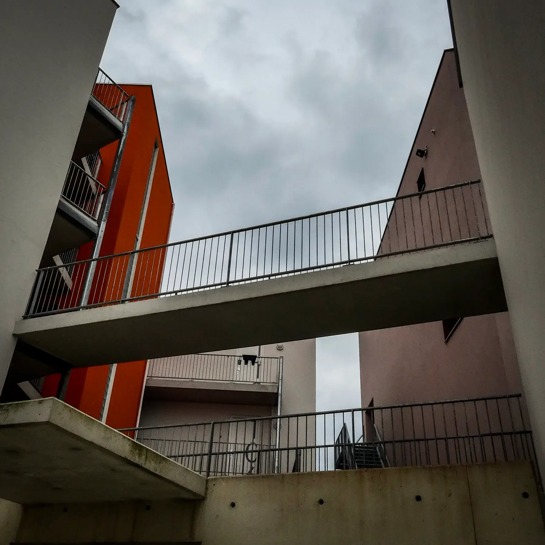 Betonnen loopbrug tussen twee gebouwen onder een bewolkte lucht, fotografie Bas Otten