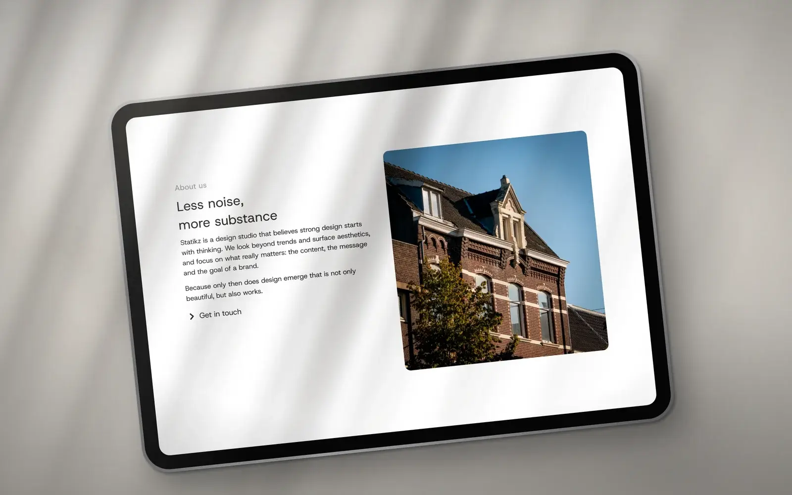 Blok Less noise, more substance van Statikz op een tablet, naast een foto van een bakstenen gevel